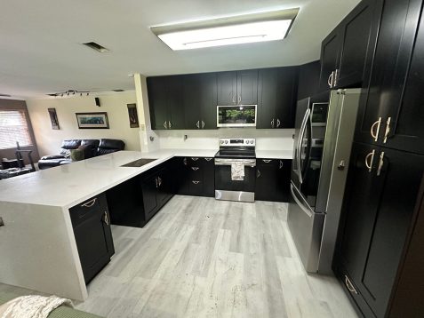 Modern kitchen featuring sleek black cabinets, stainless steel appliances, a white countertop, and a spacious layout with ample lighting.