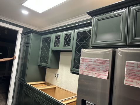 A partially installed kitchen featuring dark green cabinets, an empty space for a fridge, and protective stickers on stainless steel appliances.