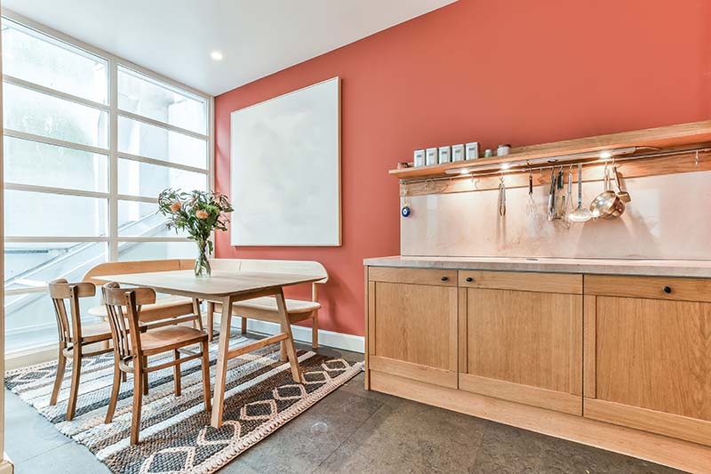 Interior painting in warm terracotta in warm terracotta with natural wood kitchen cabinetry and dining table.