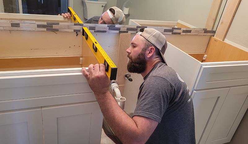 Man using a level to ensure precise bathroom cabinet installation.